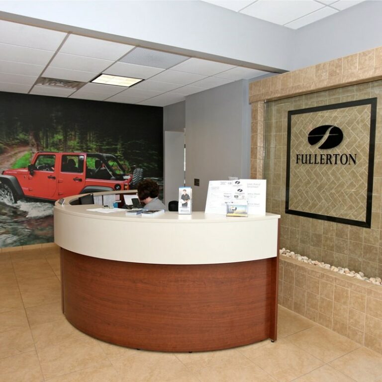 Front desk and signage in the interior of a car dealership. Big photo of a Jeep in the background.
