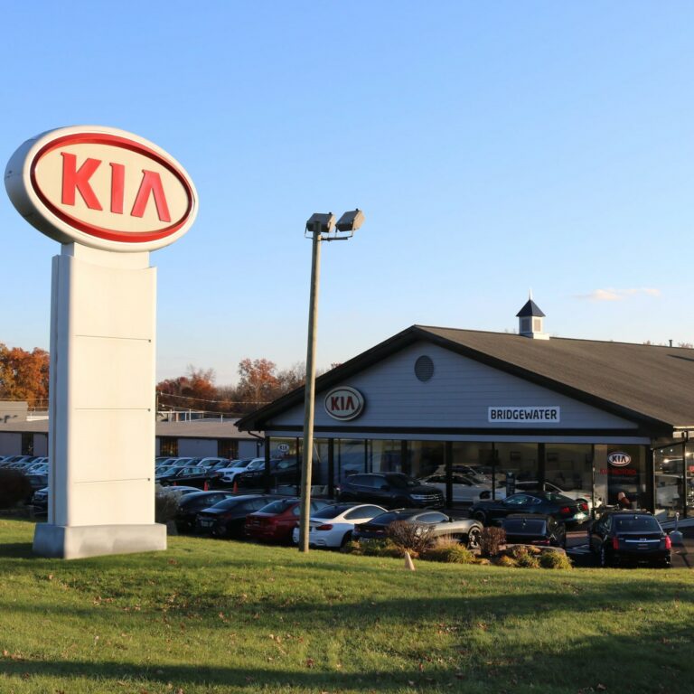 Picture of signage and front of a Kia dealership with blue skies above.
